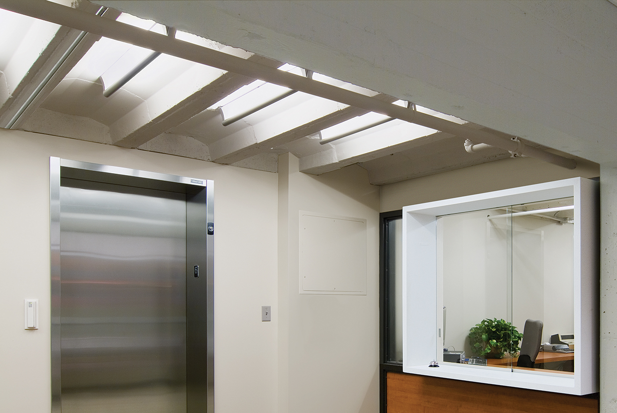 A surface mounted linear luminaire with a body that curves into the base with hidden indirect lighting shown at an elevator