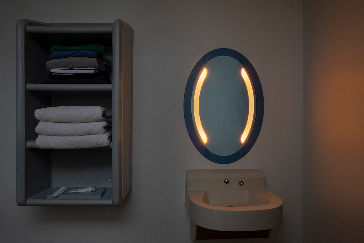 Sole oval illuminated mirror in a behavioral health/high abuse bathroom with nightlight mode on