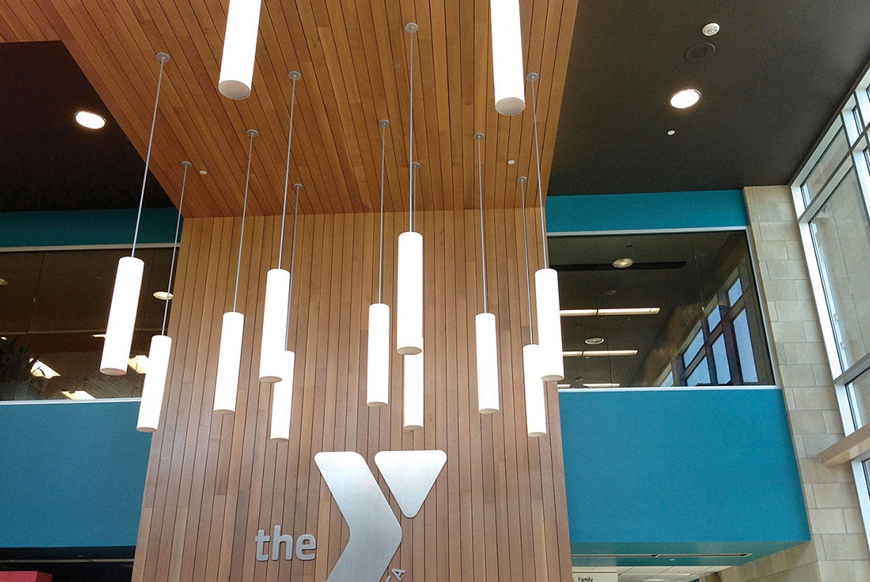 Sequence modern lighting fixtures illuminate a wood-paneled YMCA entryway. 